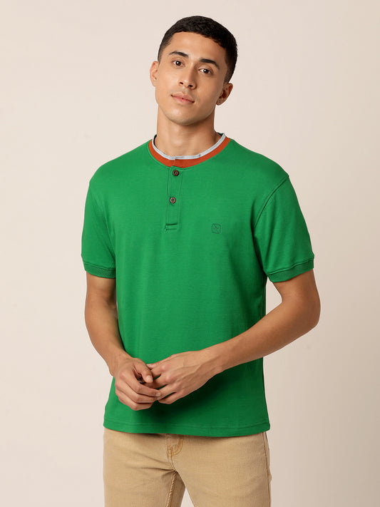A young man stands against a plain background, wearing an Abundant Green Henley T-Shirt made from organic cotton by Northmist and beige pants. He has short dark hair and a neutral expression, with one hand resting casually by his side and the other slightly raised near his waist.