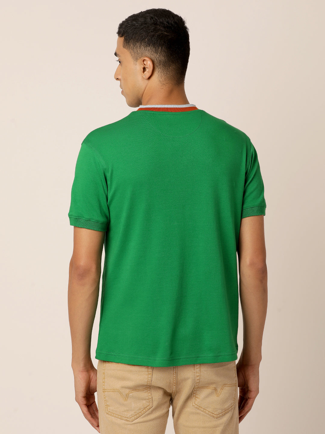 A person with short hair is facing away from the camera, wearing an Abundant Green Henley T-Shirt by Northmist and beige pants. The background is plain and light-colored.